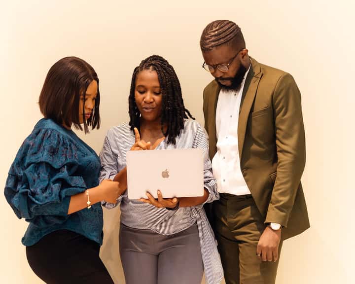 Three colleagues in an office in Lagos reviewing work on a laptop